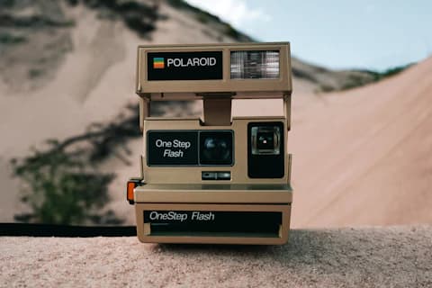 Un appareil photo instantané ancien posé sur un mur devant des dunes.