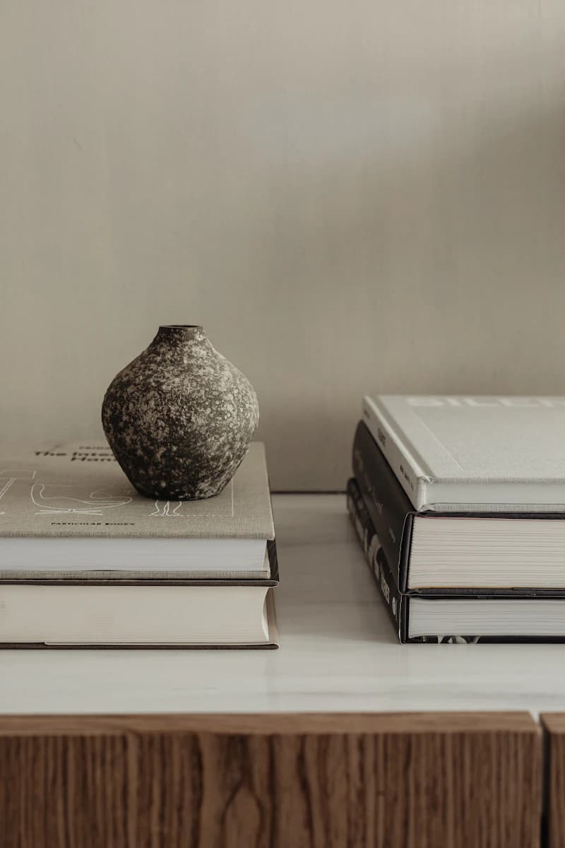 Un vase en céramique texturée sur une pile de livres aux tons neutres.