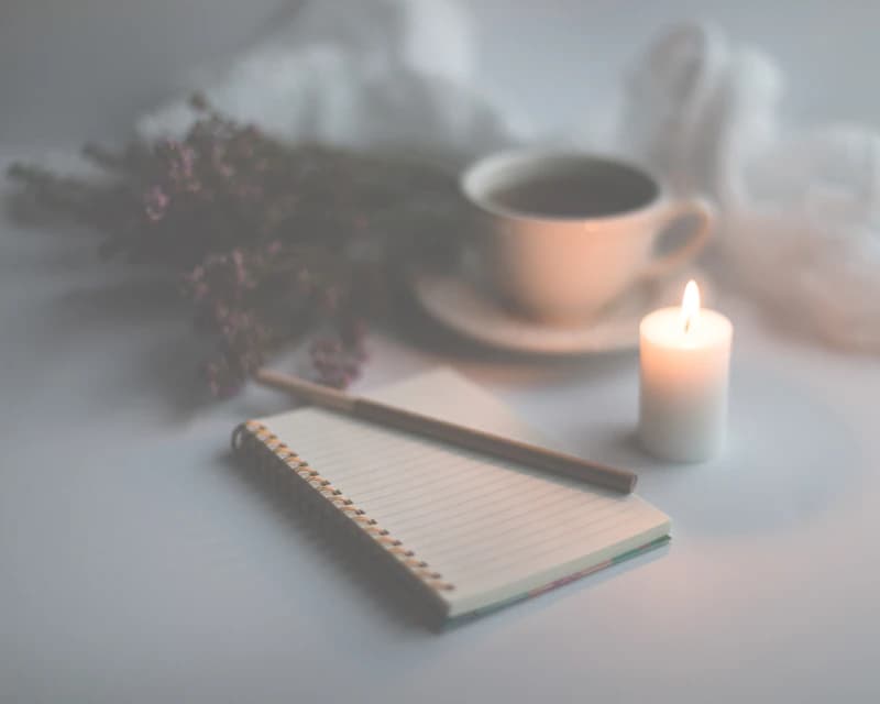 Un carnet à spirale ouvert près d’une chandelle allumée et d’une tasse.