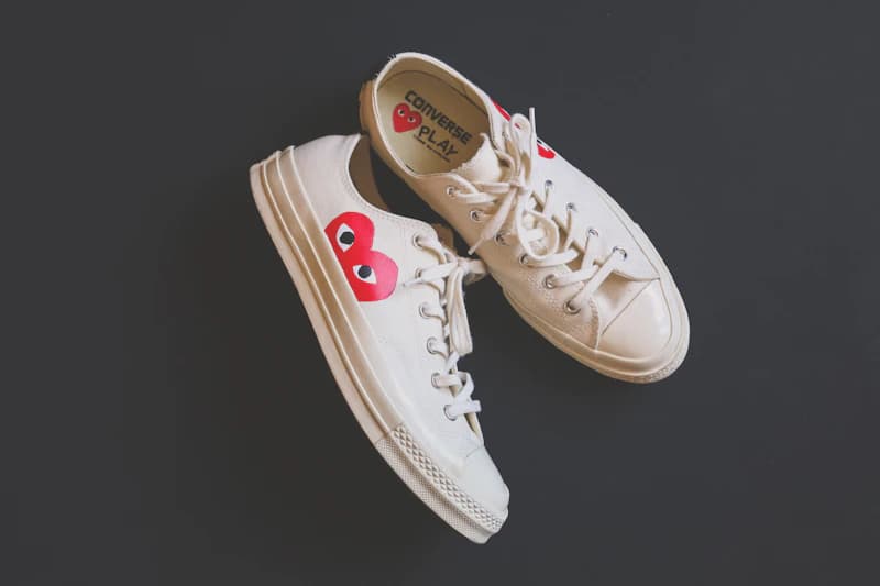 Des chaussures de sport crème ornées de cœurs rouges sur un fond sombre.